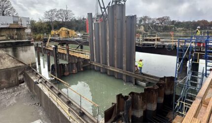 Construction workers installing steel sheet piles for the coffer dam at Lake McQueeney Dam Renovation, creating a dry work area for the renovation project